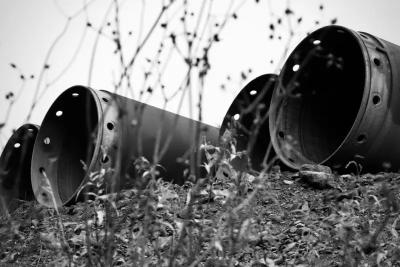 Monochrome image of large industrial pipes lying on a rocky outdoor landscape.